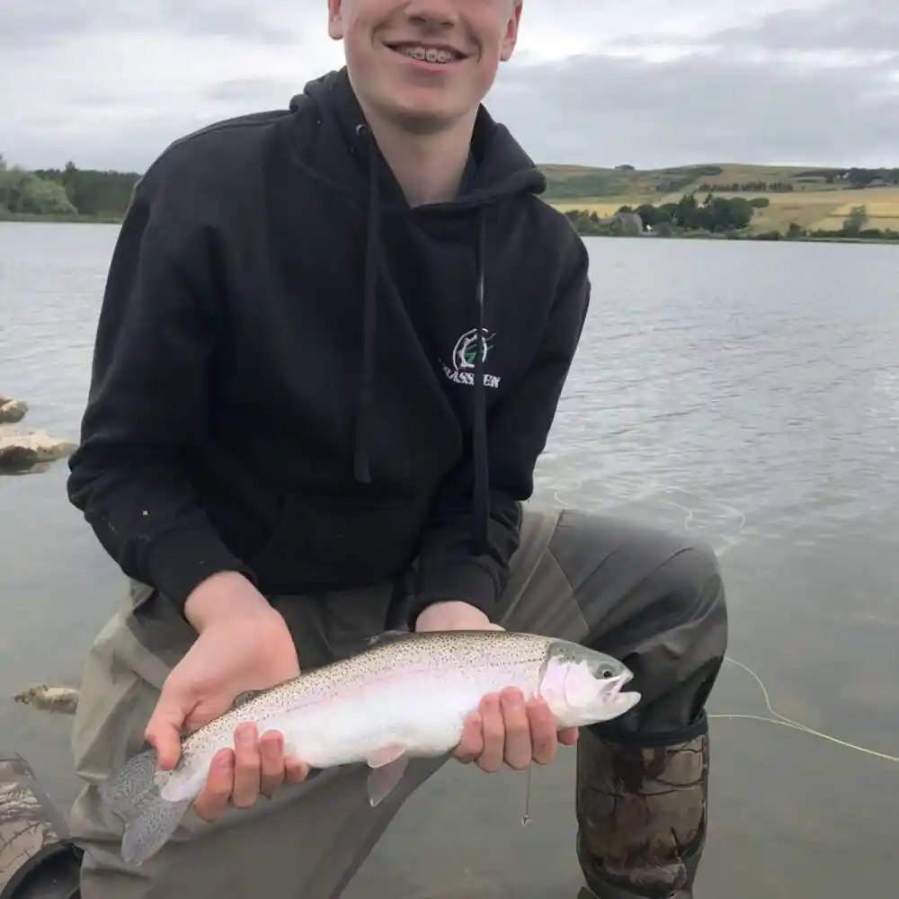 FLY FISHERMAN CATCHING FISH IN SHOAL WATER TROUT FISHING IN LOCH